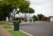 Rubbish bin with red lid and recycling bins on the street.